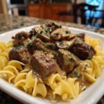 A close-up of tender beef stroganoff with sautéed mushrooms in a creamy sauce, served over egg noodles and garnished with parsley.