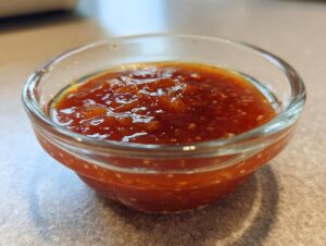 Close-up of a small glass bowl filled with a vibrant red, chunky Dumpling Sauce.