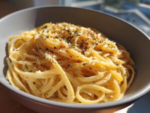 A close-up of a bowl of creamy lemon pasta, topped with herbs and red pepper flakes.