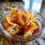 Close-up of dumplings coated in a glossy, spicy dumpling sauce with sesame seeds.