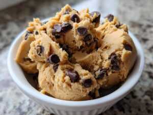 A close-up of a white bowl filled with delicious high protein cookie dough studded with chocolate chips.