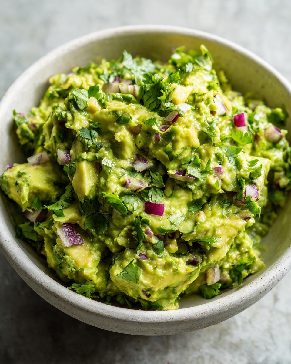 A close-up of vibrant green homemade guacamole, generously mixed with chopped red onion and fresh cilantro, served in a rustic bowl.