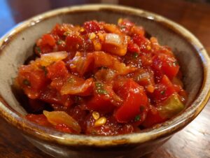 Close-up of a rustic bowl filled with vibrant, chunky homemade salsa made with tomatoes, onions, and herbs.