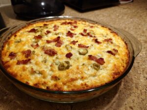 A bubbling hot Jalapeño Popper Dip topped with melted cheese and crispy bacon bits in a glass baking dish.