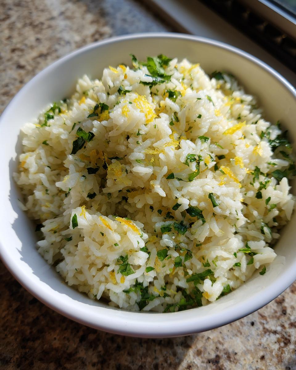 Close-up of a white bowl filled with fluffy Mediterranean lemon rice, garnished with fresh parsley and lemon zest.