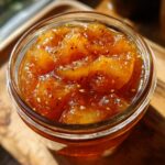 Close-up of a glass jar filled with glistening pear preserves, showing chunks of pear and seeds.