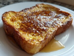A golden-brown slice of protein french toast dusted with powdered sugar and drizzled with syrup on a white plate.