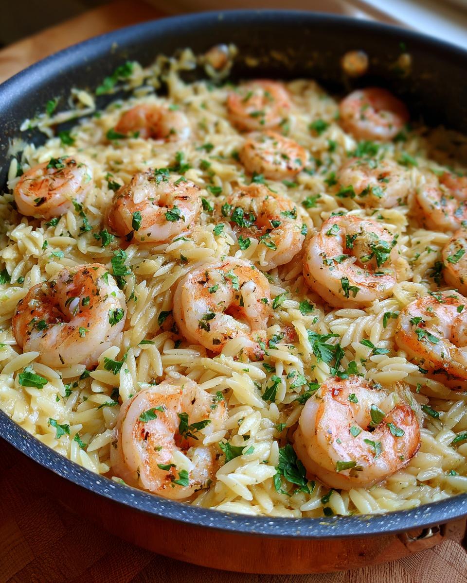 Close-up of shrimp orzo in lemon garlic sauce, garnished with fresh parsley, in a black skillet.