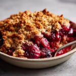 A close-up of a bowl filled with warm sour cherry crisp, featuring a golden brown crumble topping and juicy cherries.