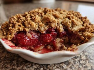 A close-up of a serving of sour cherry crisp, showing the juicy red cherries and golden brown crumble topping.