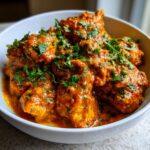 A close-up of tender chicken pieces coated in a rich, creamy orange sauce, garnished with fresh cilantro. This is our amazing butter chicken.