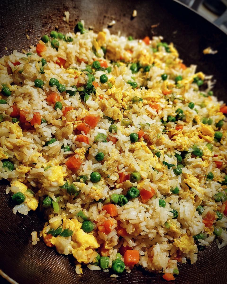 Close-up of delicious fried rice with peas, carrots, and scrambled egg in a wok.