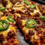 A close-up of delicious nachos topped with seasoned ground beef, melted cheese, and fresh jalapeno slices.