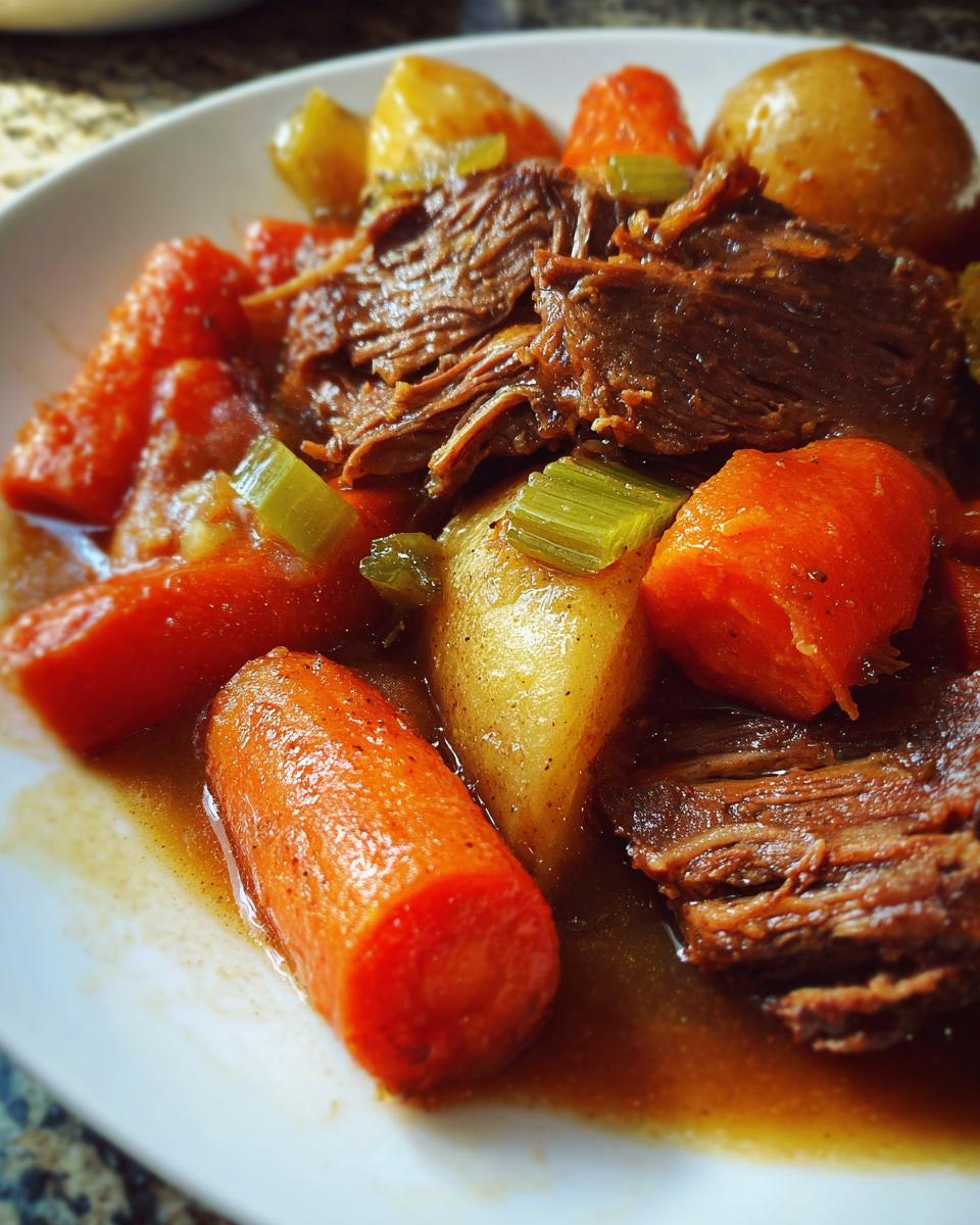 A close-up of a comforting plate of pot roast, featuring tender shredded beef, chunks of carrots, and potatoes in a rich gravy.