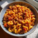 A close-up, overhead view of a bowl filled with delicious American goulash, featuring elbow macaroni and seasoned ground beef in a rich tomato sauce.