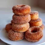 A close-up of a stack of freshly made apple cider donuts, coated in cinnamon sugar.