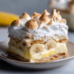 A close-up of a slice of authentic banana pudding, featuring layers of vanilla pudding, banana slices, wafers, and toasted meringue.