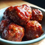 Close-up of a bowl filled with glistening BBQ meatballs coated in a rich, savory sauce.