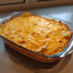 A bubbly and cheesy Buffalo chicken dip in a glass baking dish, with tortilla chips peeking out.