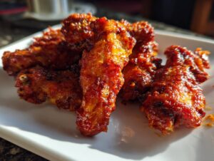 Close-up of a pile of crispy, saucy buffalo wings on a white plate, ready to be enjoyed.