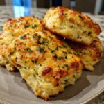A close-up of golden-brown Cheddar Bay biscuits topped with melted cheese and fresh parsley.