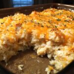 A close-up of a freshly baked chicken and rice casserole topped with melted cheddar cheese and sprinkled with parsley.