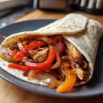 A close-up of a delicious chicken fajitas wrap filled with seasoned chicken, bell peppers, and onions.