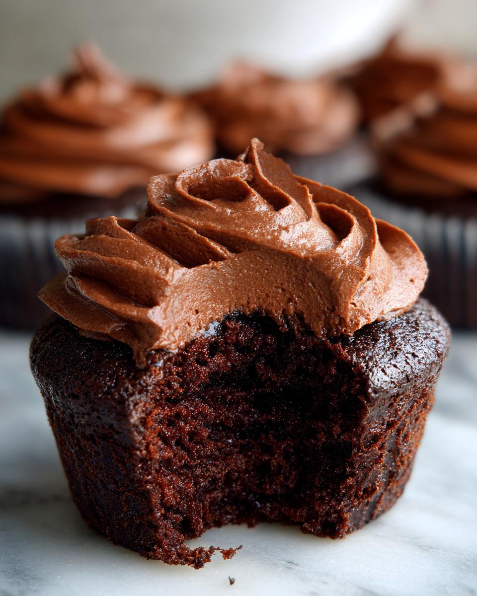 Close-up of a delicious chocolate cupcake with a bite taken out, revealing moist cake and rich chocolate frosting.