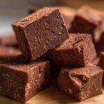 A stack of rich, dark chocolate fudge squares dusted with cocoa powder.