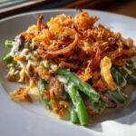 A close-up of a serving of classic green bean casserole topped with golden fried onions.