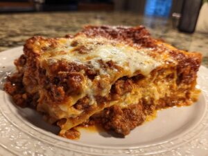 A generous slice of classic lasagna on a white plate, featuring layers of pasta, rich meat sauce, and melted cheese.
