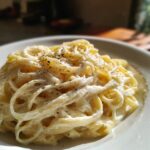 A close-up of a plate piled high with creamy Fettuccine Alfredo, generously seasoned with freshly cracked black pepper.