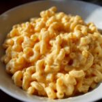 A close-up of a bowl filled with creamy vegan mac and cheese, showing the elbow macaroni coated in a rich, golden sauce.