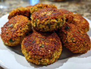 A close-up shot of a plate filled with golden-brown, crispy falafel patties, showcasing their textured exterior and green herb flecks.
