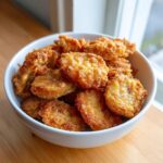 A white bowl filled with golden-brown, crispy fried pickles, ready to be enjoyed.