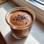 A close-up of rich chocolate mousse in a glass, topped with chocolate shavings.