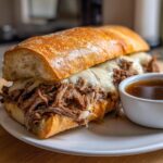 A delicious French dip sandwich overflowing with shredded beef and melted cheese, served with a side of au jus.