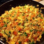 Close-up of a pan filled with freshly made fried rice, featuring scrambled eggs, peas, and diced carrots.