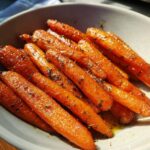Close-up of a bowl filled with vibrant, tender glazed carrots, sprinkled with herbs.