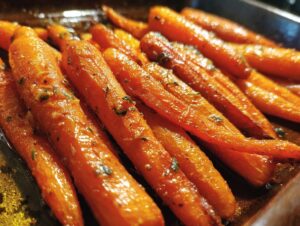 Close-up view of perfectly glazed carrots, glistening with a sweet sauce and sprinkled with fresh herbs.