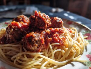 A close-up of tender spaghetti and meatballs in rich tomato sauce on a floral plate.