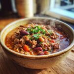 A steaming bowl of hearty beef chili, packed with ground beef, kidney beans, and tomatoes, garnished with fresh parsley.