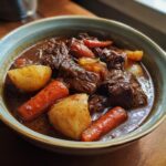 A close-up of a bowl of hearty beef stew, featuring tender chunks of beef, potatoes, and carrots in a rich gravy.