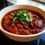 A close-up of a white bowl filled with hearty vegetarian chili, topped with fresh cilantro.