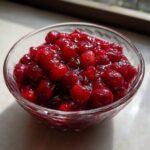 Close-up of glistening homemade cranberry sauce in a clear glass bowl, showcasing whole cranberries.