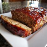 A close-up of a slice of juicy meatloaf topped with a shiny glaze, ready to be served.