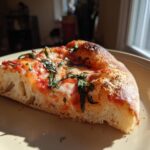 A close-up of a slice of authentic Margherita pizza, featuring melted mozzarella, tomato sauce, and fresh basil leaves.