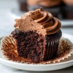 A close-up of a delicious chocolate cupcake with rich chocolate frosting, partially eaten.