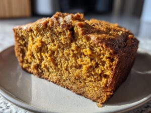 A close-up of a moist slice of pumpkin bread on a grey plate, showcasing its texture and golden-brown crust.
