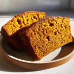 Two moist slices of pumpkin bread served on a plate, showing the rich orange color and tender crumb.